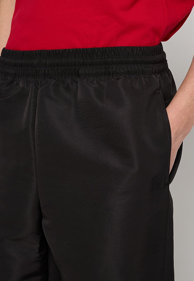 Schwarze Hose mit elastischem Bund aus einem glatten, leichten Stoff mit lockerer Passform und Seitentaschen. Die Textur ist leicht glänzend.