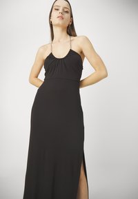 Czarna maxi sukienka z marszczonym biustem, cienkimi ramiączkami i bocznym rozcięciem, wykonana z gładkiego, lekkiego materiału dla eleganckiego wyglądu.