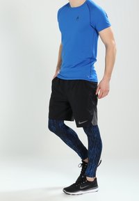 Blå kortärmad träningsskjorta, svarta shorts och blå mönstradeleggings. Svarta sneakers med vita detaljer.