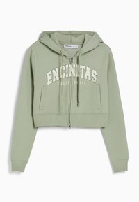 Sudadera con cremallera recortada en verde claro con una textura suave. Presenta bolsillos tipo canguro en la parte delantera y el texto "ENCINITAS CALIFORNIA" en blanco.