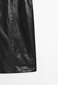 Jupe en mesh noire avec une surface douce et texturée, présentant une coupe évasée et une longueur sous le genou. Apparence légère et semi-transparente.