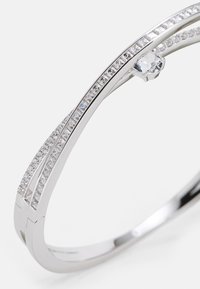 Silbernes Armband mit zwei gebogenen Bändern, verziert mit klaren und diamantenähnlichen Steinen, die einen klaren, zentralen Stein hervorheben. Glatte, polierte Oberfläche.