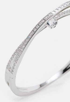 Silbernes Armband mit zwei gebogenen Bändern, verziert mit klaren und diamantenähnlichen Steinen, die einen klaren, zentralen Stein hervorheben. Glatte, polierte Oberfläche.