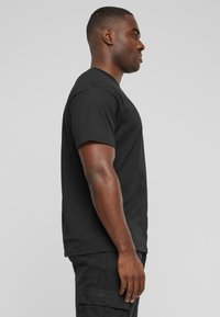 Czarny t-shirt z krótkim rękawem, z dekoltem okrągłym, wykonany z bawełny. Gładka faktura z prostym krojem, noszony z ciemnymi szortami cargo.