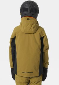 Žlutozelená nepromokavá bunda s kapucí, černé boční panely a logo "HELLY HANSEN" na zadní straně. V doprovodu černých rukavic a helmy.