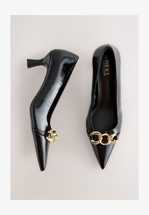 Zwarte lakleren hoge hakken met puntige neus. Gouden kettingdetail aan de voorkant. Gladde textuur met een glanzende afwerking, voorzien van een hak van gemiddelde hoogte.