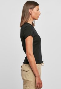Svart kortermet topp med volanger, tettsittende design og rund hals. Kombinert med khaki cargobukser med sidelommer.
