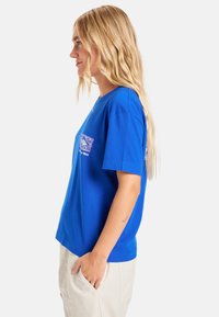 Royalblaues Baumwoll-T-Shirt mit kurzen Ärmeln und Rundhalsausschnitt, mit einem grafischen Logodesign auf der Vorder- und Seite. Schlichte Rückseite.
