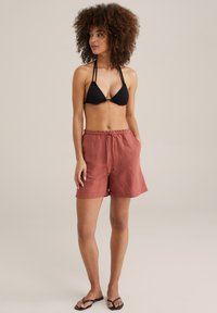 Črni bikini vrh v obliki trikotnika z tankimi naramnicami, v kombinaciji z ohlapnimi lanenimi kratkimi hlačami v rjavi barvi do kolen, ki imajo elastičen pas in žepe.