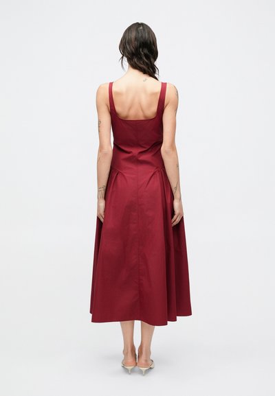 Μπορντό αμάνικο φόρεμα με εφαρμοστή κορυφή, φουσκωτή φούστα και φερμουάρ στην πλάτη. Λείο ύφασμα με ελαφριά γυαλάδα και πλαϊνές ραφές.