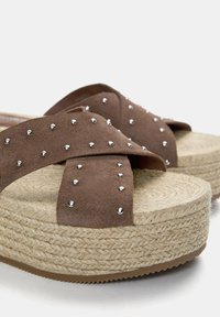 Sandali platform in suede marrone con fasce incrociate, adornati con borchie argentate, caratterizzati da una suola intermedia in juta intrecciata e una suola esterna in gomma testurizzata.