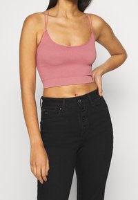 Růžová pruhovaná crop top s tenkými ramínky a přiléhavým střihem. V kombinaci s černými džíny s vysokým pasem a zapínáním na knoflík.
