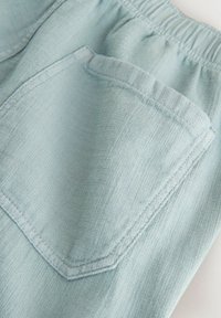 Poche en tissu texturé bleu clair sur un pantalon à taille élastique, montrant les détails des coutures et la texture du matériau doux.
