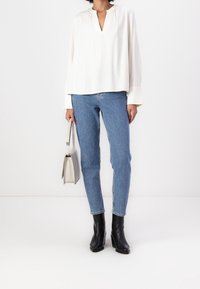 Blouse blanche à manches longues avec un col en V, associée à un jean skinny bleu et des bottines à talons noires. Présente une coupe décontractée et une texture douce.