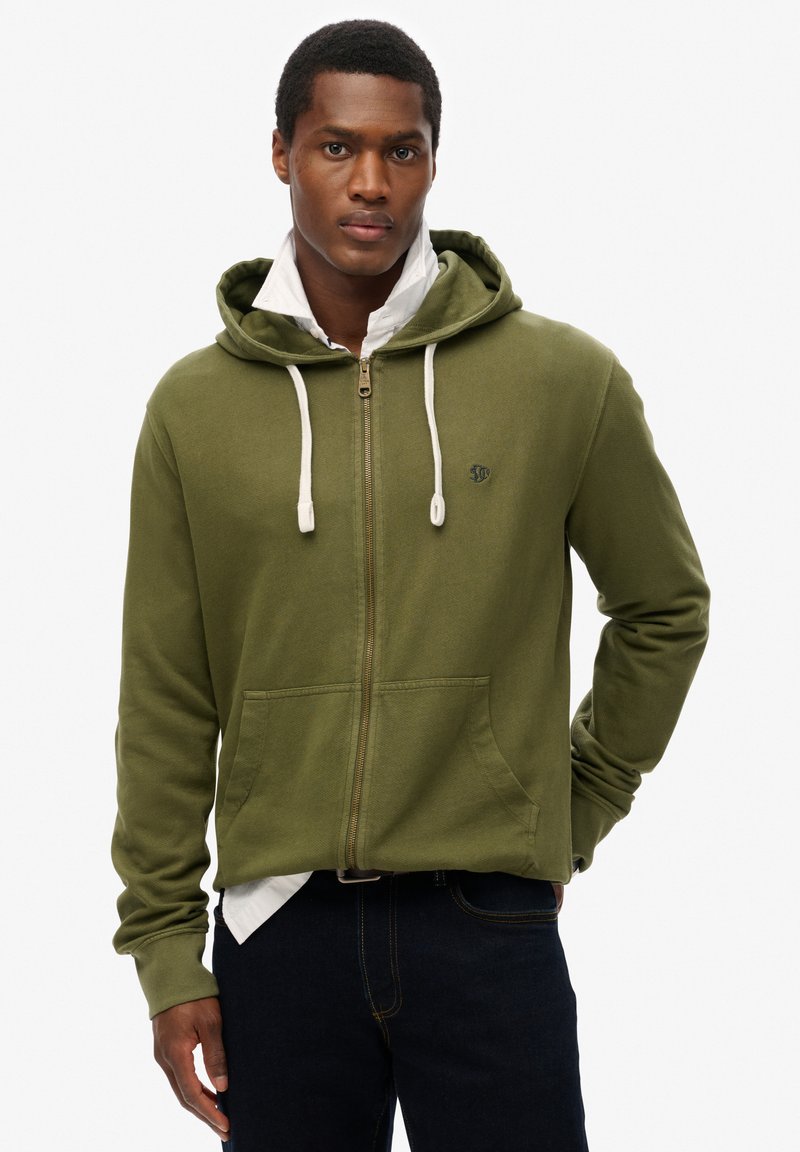 Sudadera con cremallera de color verde oliva, con capucha ajustable, bolsillos frontales, puños acanalados y un pequeño logo bordado en el pecho.