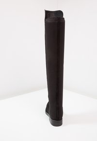 Knähöga svarta stövlar gjorda av smidigt material med platt sula, med en stilren design och vertikala sömmar längs baksidan.