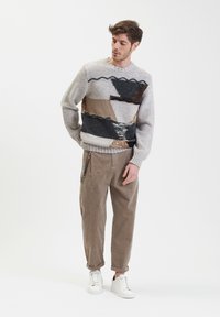 Maglione lavorato a maglia di colore grigio con motivi astratti in nero, marrone e beige. Abbinato a pantaloni in corduroy beige e sneakers bianche.
