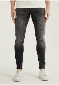 Vaqueros negros desgastados con un ajuste slim, que presentan áreas desvaídas y parches deshilachados, combinados con zapatillas blancas.