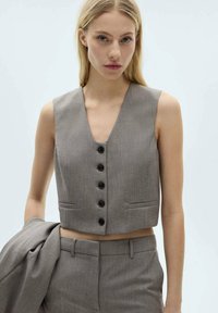 Grijze cropped vest van gladde stof, met een V-halslijn, zes donkere knopen en twee kleine voorzakken.