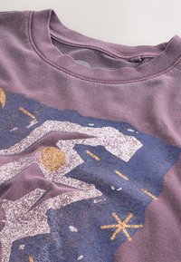 Lila sweatshirt med grafisk design i guld och blått, texturerade detaljer och rund halsringning.