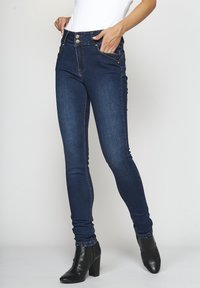 Smala jeans i mörkblå denim, med hög midja, två guldknappar, fickor med dekorativ sömnad och subtila blekningsdetaljer.