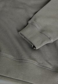 Szara bluza z prążkowanym mankietem i ściągaczem, o miękkiej fakturze i minimalistycznym designie. Na krawędziach widoczne są przeszycia.