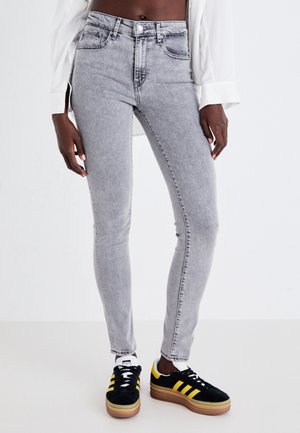 Grå højtaljede skinny jeans med blød tekstur, detaljerede syninger, fem lommer og knaplukning, kombineret med sorte og gule sneakers.