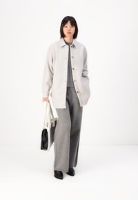 Camicia giacca in lana grigia chiara con bottoni, top in maglia grigia, pantaloni larghi in lana grigia, stivaletti neri alla caviglia e una borsa a spalla bicolore.