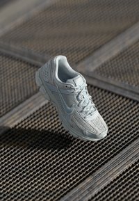 Shoe de corrida Nike azul claro com parte superior em malha, língua acolchoada e sola texturizada, exposta contra uma superfície padronizada.