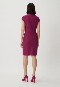 Fuchsia Kurzarmkleid mit tailliertem Oberteil, knielangem Saum und Rückenschlitz. Getragen mit passenden High Heels, glatter Stoffstruktur.