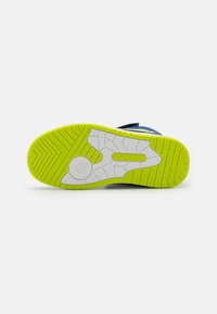 Schuhsohle mit multidirektionalen Rillen, ausgestattet mit einer gelb-grünen Gummisohle und einer weißen Zwischensohle, die ein kreisförmiges Logo in der Mitte aufweist.