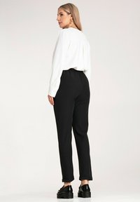 Biała bluzka z długim rękawem w połączeniu z czarnymi spodniami z elastycznym pasem, o luźnym kroju i podwijanych mankietach; noszona z czarnymi butami na platformie.