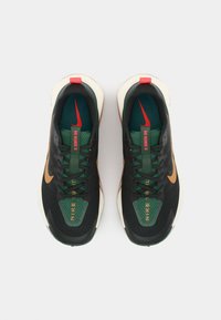 Chaussures de sport noires et vertes avec tige en maille, accents rouges et semelle extérieure brune ; elles présentent un logo Nike bien en vue sur la langue et sur les côtés.