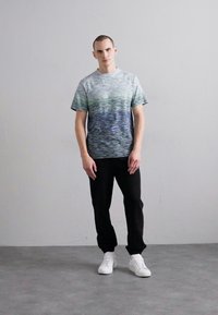 Kortermet t-skjorte i blå-grønn gradientmønster, pairert med svarte bukser og hvite sneakers. Glatt stoff med avslappet passform.