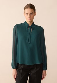 Teal long-sleeve blouse with a ruffled collar and tie detail, made from lightweight fabric with a flowing silhouette and elastic cuffs.