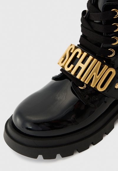 Must must nahkboots, millel on paks kummitald, silmapaistva kuldse logo rihmaga ja mustade paeltega. Sile tekstuur, julge disain.