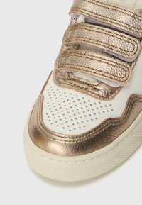 Metallisk gull- og hvit sneakers med tre borrelåsremmer, teksturert detaljering, perforerte områder og gummisåle.