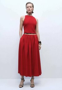 Completo rosso in due pezzi con top cropped senza maniche e una gonna fluida, al ginocchio, con vita arricciata e texture liscia.