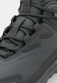 Gray hiking shoe featuring a textured mesh upper, reinforced overlays, and thick rubber sole with visible tread pattern. Adjustable laces included.