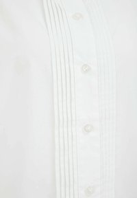 Biely košeľový dres s vertikálnymi záhybmi pozdĺž légy, šiestimi priehľadnými gombíkmi a ostrou, hladkou textúrou látky.