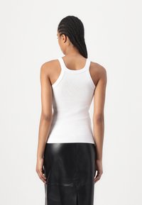 Witte geribbelde tanktop met brede schouderbanden en een aansluitend ontwerp. Geselecteerd met een zwarte leren rok met een rechte snit en een centrale split.