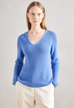 Pulover tricotat de culoare albastru deschis, cu guler în V, textură cordistă și mâneci lungi. Puloverul are deschideri laterale la tiv și este asortat cu pantaloni de culoare crem.