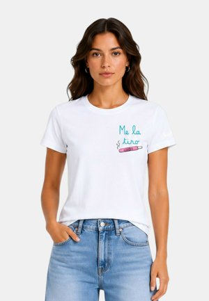 Donna con lunghi capelli mossi indossa una t-shirt bianca con testo verde acqua e illustrazione rosa di un test di gravidanza, abbinata a jeans azzurri chiari.