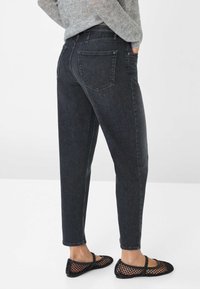 Jean noir taille haute avec une jambe fuselée, design à cinq poches et détails de décoloration subtils, associés à des ballerines en mesh noir.