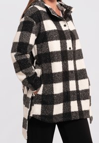 Černobílá kostkovaná fleecová košile s límcem, zapínáním na knoflíky a postranními kapsami. Měkká textura s volným střihem.