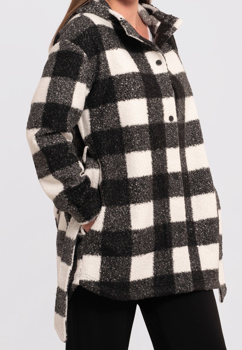 Černobílá kostkovaná fleecová košile s límcem, zapínáním na knoflíky a postranními kapsami. Měkká textura s volným střihem.