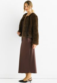 Brown faux fur jacket with a cropped design, worn over a dark brown satin skirt. Black pointed flats complete the outfit.