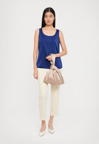 Navy sleeveless blouse, cream cropped pants, beige knot bag, and pointed white shoes. Smooth fabric and minimalist design.