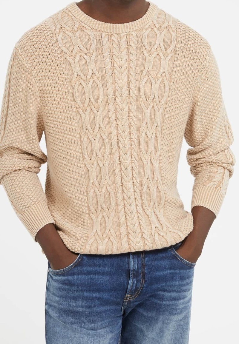 Beiger Strickpullover mit Zopfmuster in der Mitte und strukturierten seitlichen Einsätzen. Gerippte Bündchen und Ausschnitt mit sichtbaren Nahtdetails.