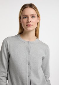 Ljusgrå cardigan gjord av mjukt tyg, med rund halsringning, knapplist och långa ärmar med en slät yta.